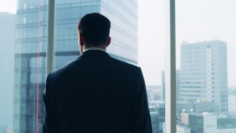 Medium Shot of Successful Businessman wearing a Suit Standing in His Office, Contemplating Next Big Business Deal, Looking out of the Window. 