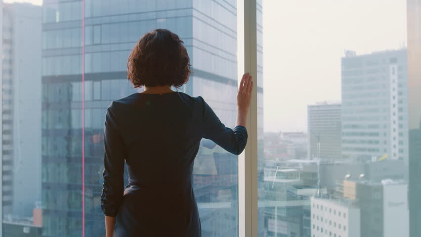 Back View Shot of Successful Businesswoman in the Striking Black Dress Standing in Her Office and Looking out of the Window Thoughtfully.  Royalty-Free Stock Footage #1014231629