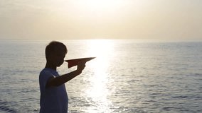 Closeup view of paper airplane in hand of person isolated on sunny sunset sky and sea water background.  Dreaming about travelling concept. Video shoot at golden hour on summer morning.