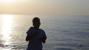 Cute little funny kid listen to music and dancing at sunset or sunrise summer beach isolated on sunny sea and sky background. Real time full hd video footage.