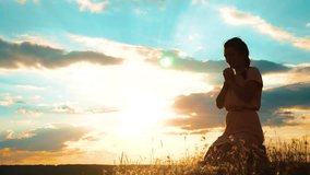 Girl folded her lifestyle hands in prayer silhouette at sunset. woman praying on her knees. slow motion video. Girl folded her hands in prayer pray to God. the girl praying asks forgiveness for sins