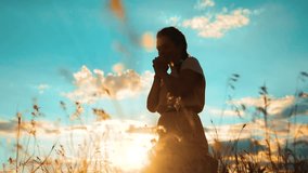 Girl folded her hands in prayer silhouette at sunset. woman praying on her knees. slow motion video. Girl folded her hands in prayer pray to God. the girl praying asks forgiveness for sins of