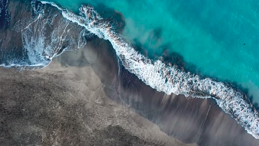 Top view of a deserted black volcanic beach. Coast of the island of Tenerife. Aerial drone footage of sea waves reaching shore