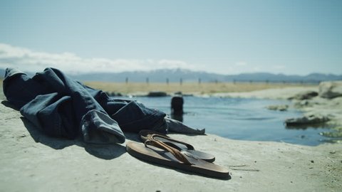 Close up of flipflops and jeans with woman skinny dipping in background / Meadow, Utah, United States