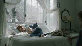 Slow motion of girl climbing into bed and cuddling with mother near bay window / Pleasant Grove, Utah, United States