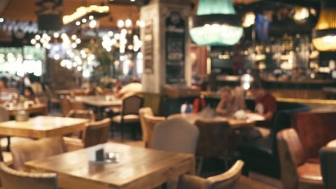 Blurred image of the interior of a large beautiful restaurant with bright lighting. A happy family with a child is sitting at a restaurant at a table, having dinner, talking. Defocussed interior