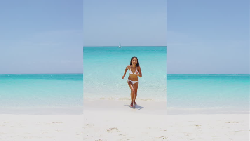 Vertical videos. Sun vacation travel, excited woman jumping at beach on sunny day. Cheerful young female in white bikini is enjoying her summer vacation. Idyllic view of seascape against sky.