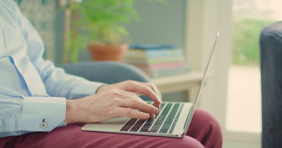 Handheld shot of male businessman using laptop. Entrepreneur is sitting on sofa with laptop while typing. He is working at home. Shot on RED Camera.  | Shutterstock HD Video #1014245054