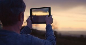 Man photographing beautiful sunset. Handheld shot of male is holding digital tablet. He is standing against cloudy sky. Shot on RED Camera.