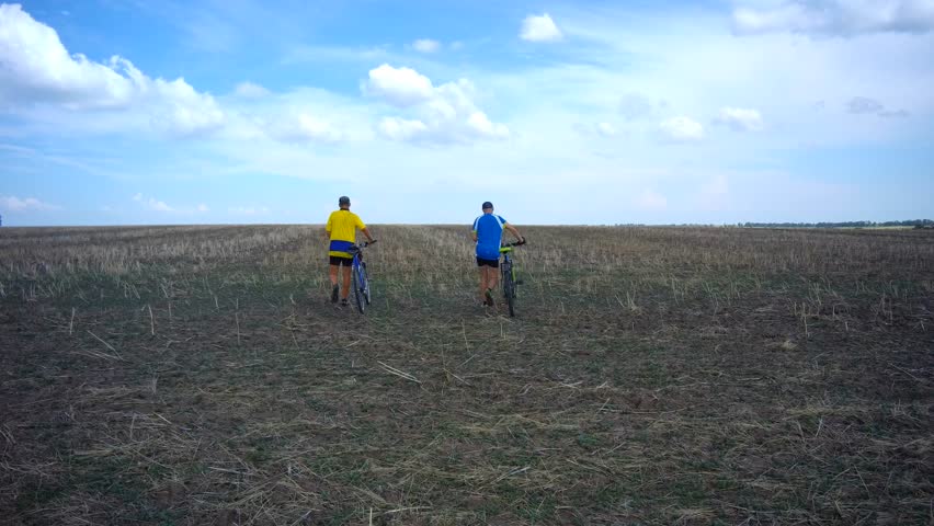 two male tourists on a bicycle traveling along the farm field