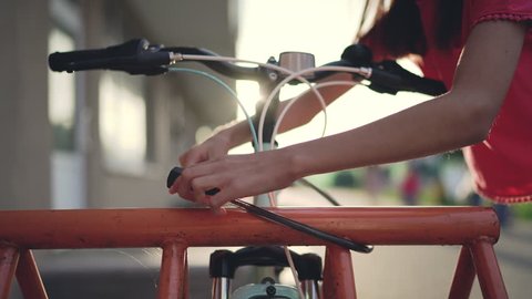 Girl fastening bicycle lock on street parking at sunset