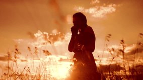 Girl folded her hands in prayer silhouette at sunset. woman praying on her knees. slow motion video. Girl folded her hands in prayer pray to God. the girl praying asks forgiveness for sins lifestyle
