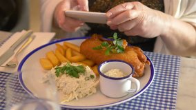 Professional video of woman taking photos of fish and chips dinner by smartphone in 4k slow motion 60fps