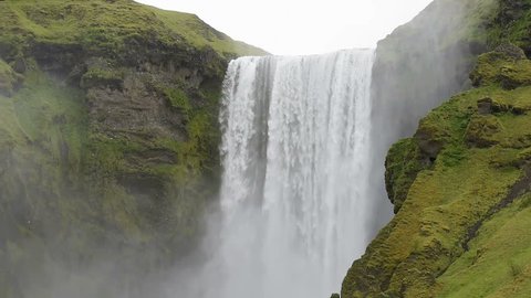 Skogafoss Skogar waterfall in Iceland with white water falling off cliff in green mossy summer, rocky landscape, nobody, raining with sound of rain drops