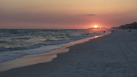 Sunset in Santa Rosa Beach, Florida, people silhouette walking in distance in panhandle with ocean gulf of mexico waves, sun path reflection in slow motion