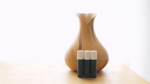 Wooden bamboo essential oil diffuser closeup, with three glass bottles, steam modern minimalistic minimal health vapor on table by window