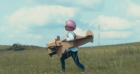 TRACKING Cute little dreamer kid girl wearing pink helmet and aviator glasses flying in a cardboard airplane through the field, pretending to be a pilot. 4K UHD 60 FPS SLO MO 