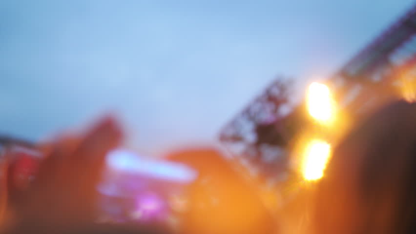 Slow motion close-up shot of man making smart phone video of outdoor concert. Music band performing in front of hundreds of people