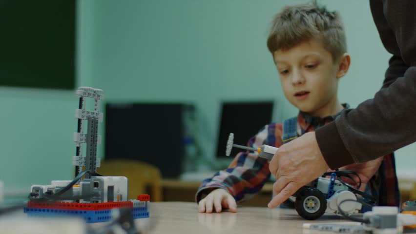 Close up shot of a teacher helping young boy with a robots in school science club. Small lego car riding on a table. Project for engineering club in school. Royalty-Free Stock Footage #1014274904