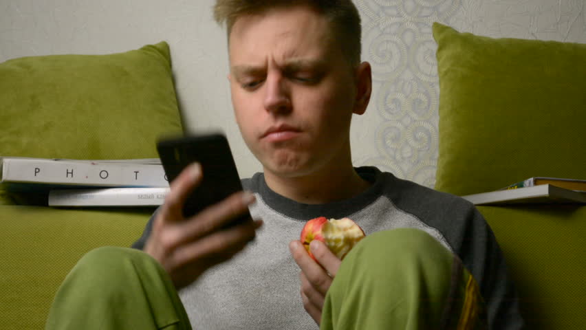 Angry, confused and frustrated young man teenager looking at mobile phone eating Royalty-Free Stock Footage #1014277733