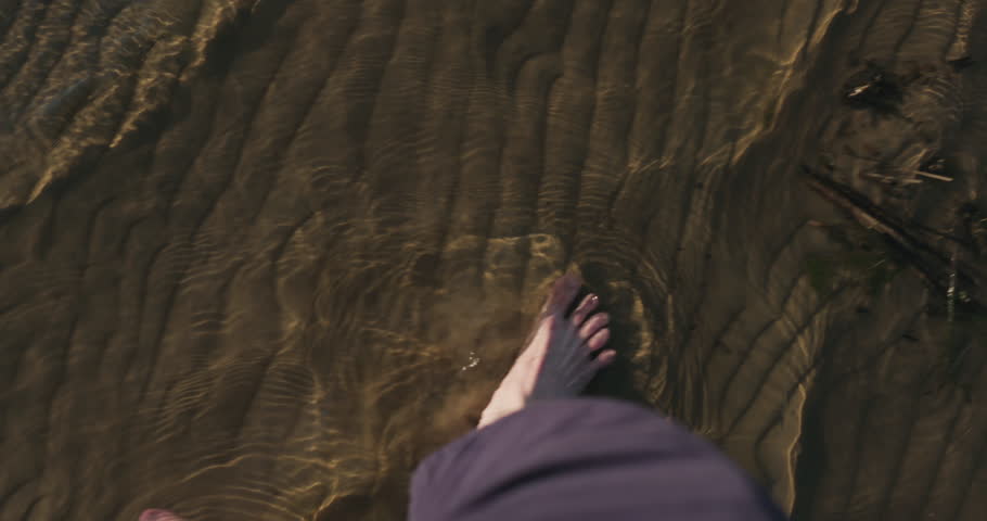 Slow motion pov view man walking barefoot in shallow water on beach