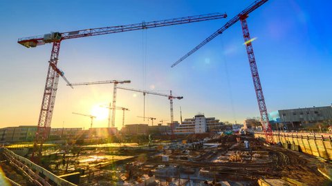 Timelapse footage of a large construction site with several busy cranes at dusk, with clear blue sky and the setting sun