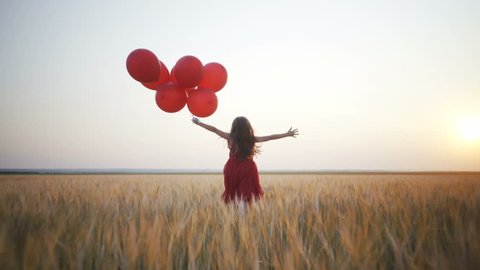 happy young girl with red balloons running in the wheat field at sunset. 4k video. Freedom concept