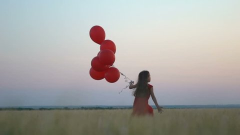 happy young girl with red balloons running in the wheat field at sunset. Slow motion 120 fps footage. Freedom concept