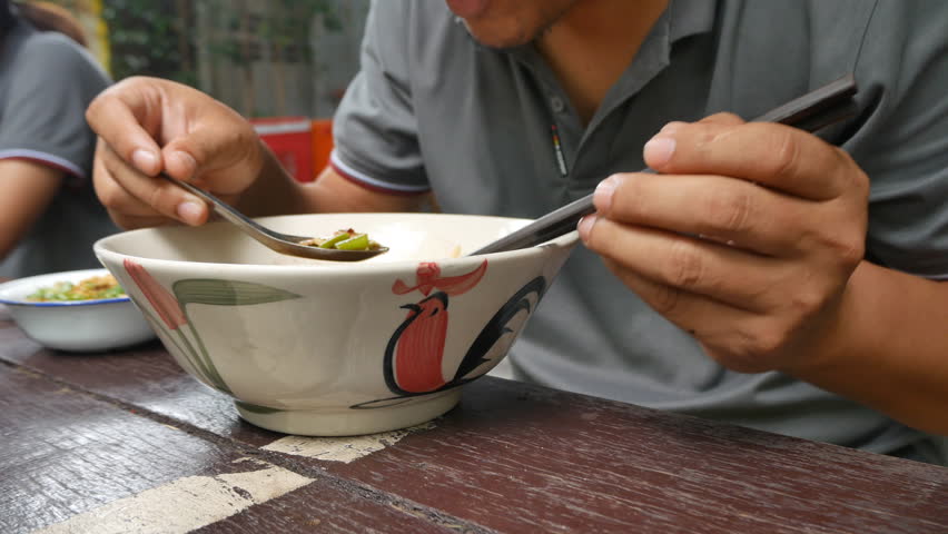 Asian man to delicious eating noodles  at outdoor restaurant. Using sticks for eat the hot traditional Chinese food