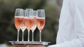 Hands of the waiter with a tray of champagne in glasses with strawberries. Slow motion