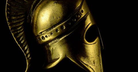 A wonderful golden spartan helmet as part of the equipment of ancient Greek soldiers. King Leonidas and his 300th The piece of metal turns against a black background, shiny and mystical.