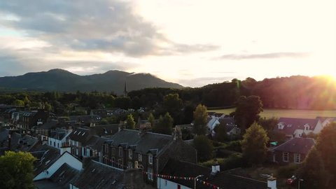 Aerial view of a little village in Scotland with beautiful sunset or sunrise. Cinematic footage of small country town with church far away in trees with mountains on background.