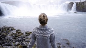 Young woman arms outstretched in front of the magnificent waterfall in Iceland, Godafoss falls. People travel exploration concept 4K video