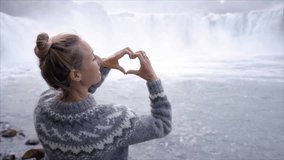 Young woman in Iceland making heart shape finger frame on spectacular waterfall loving the beauty in nature, tourism travel people concept in Northern Europe countries SLOW MOTION