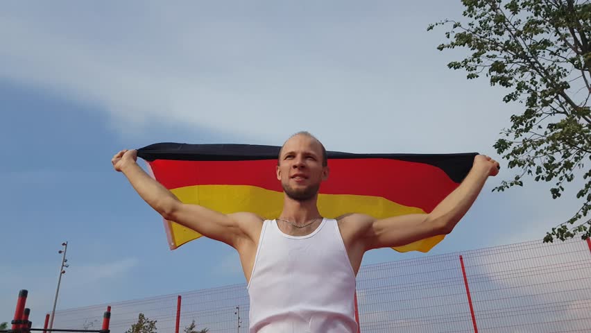Young Man Holding German National Flag To The Sky With Two Hands
