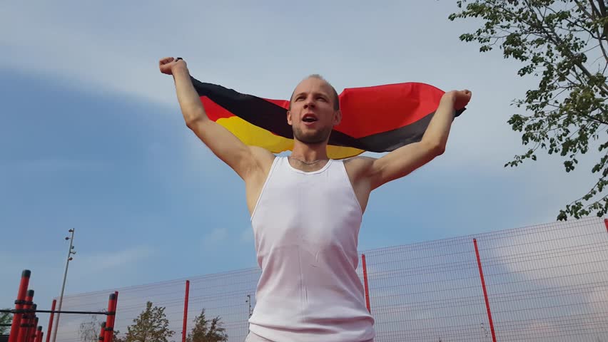 Young Man Holding German National Flag To The Sky With Two Hands