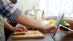 4K. woman use finger slide on tablet screen, slicing red tomato prepare ingredients for cooking follow cooking online video clip on website. cooking content on internet technology for modern lifestyle