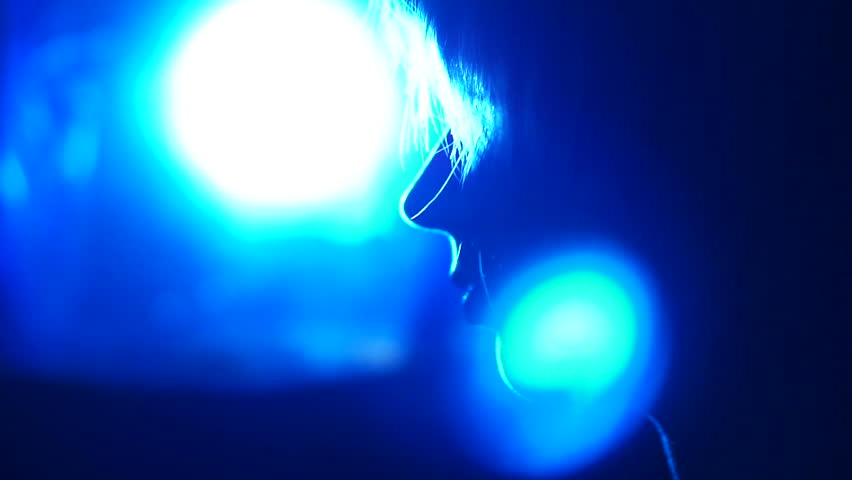 Profile silhouette of a sexy blond girl doing a stiptease and dancing, in the dark with blue light in her back and appearances of red light in her front.