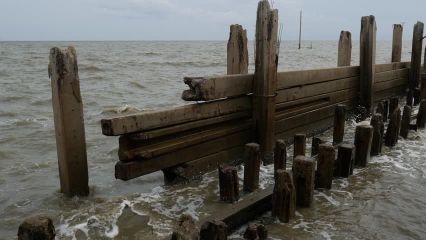 Broken sea wall and damaged pier submerged by water, concrete studs in sea, rising water