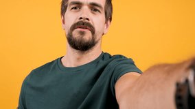 Adult bearded man vlogging with his camera on yellow orange background. Modern lifestyle