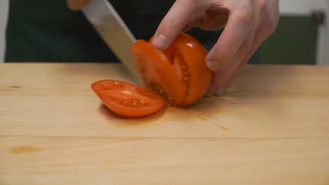 Slice Tomatoes in Half. Clip. cooking, food and home concept - close up of male hand cutting pepper on cutting board at home. close up of male hand cutting tomato