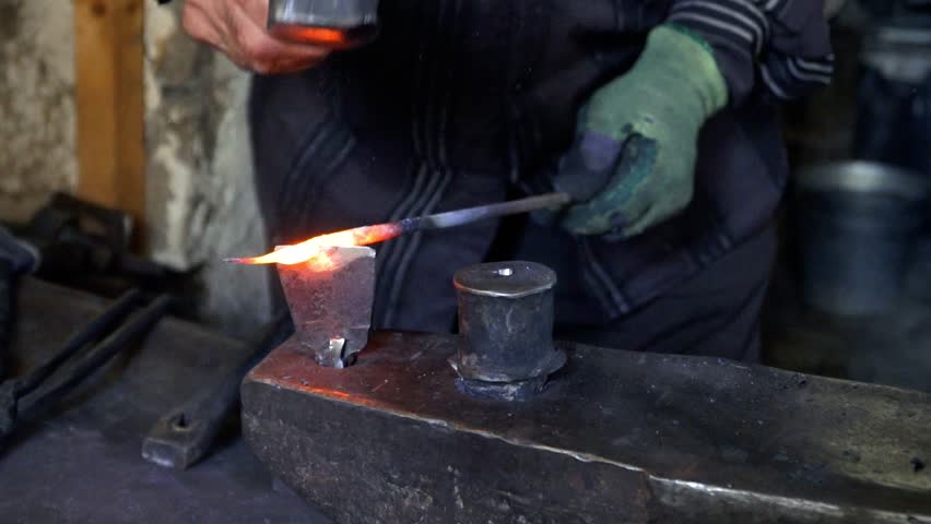 The blacksmith manually forging the molten metal on the anvil in smithy with spark fireworks. Blacksmith forging metal in slow motion. 4K