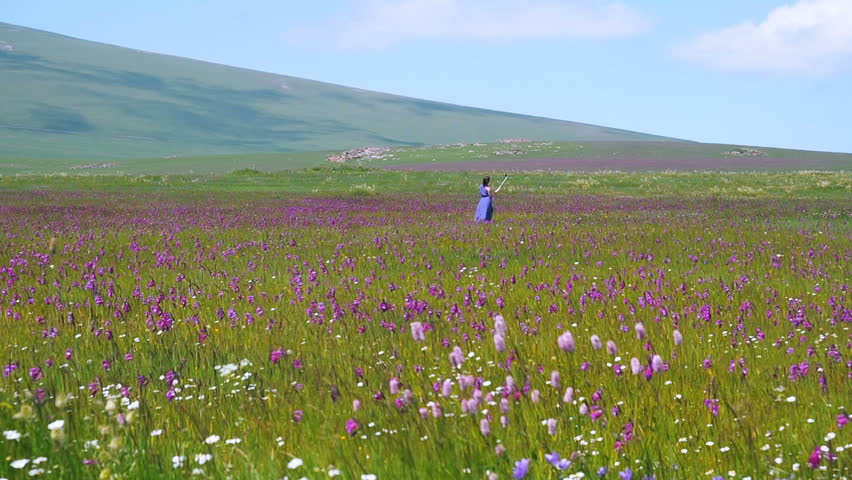 Pretty caucasian girl taking photo with a selfie stick on wonderful meadow with purple flowers. Young beautiful happy woman in a straw hat make selfie on nature background. Pretty woman outdoors. 