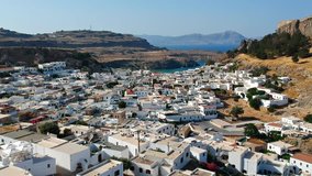 Aerial birds eye view drone video of village Lindos, Rhodes island, Dodecanese, Greece. Sunset panorama with castle, Mediterranean sea coast. Famous tourist destination in South Europe.