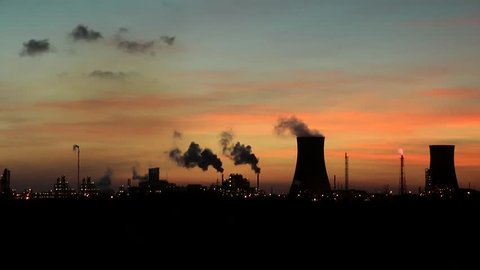 Cooling towers at oil refinery with steam. Sun setting sky time lapse