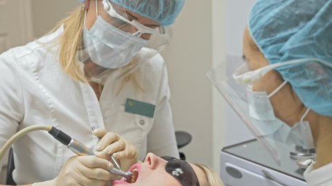 Dentist is treating a patient in a modern dental office. Orthodontist works with an assistant. The operation is carried out using a cofferdam. The client is inserted and restored teeth, make a denture