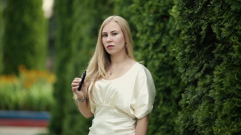Vape teenager. A young cute white girl in a dress is vaping an electronic cigarette  on the street in summer.