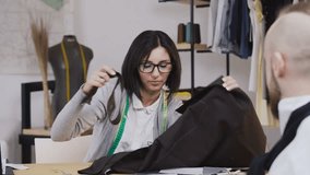 Young woman fashion designers and her customer working with fabrics sitting at the beautiful office with different tailoring tools on the table. Two people fashion designers choosing fabric at the