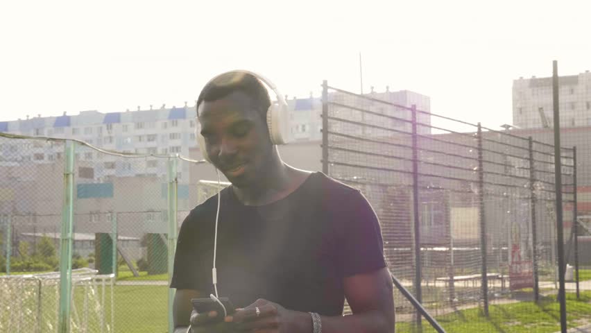 Black man running and listening to music in urban background. Handsome male doing workout outdoors.