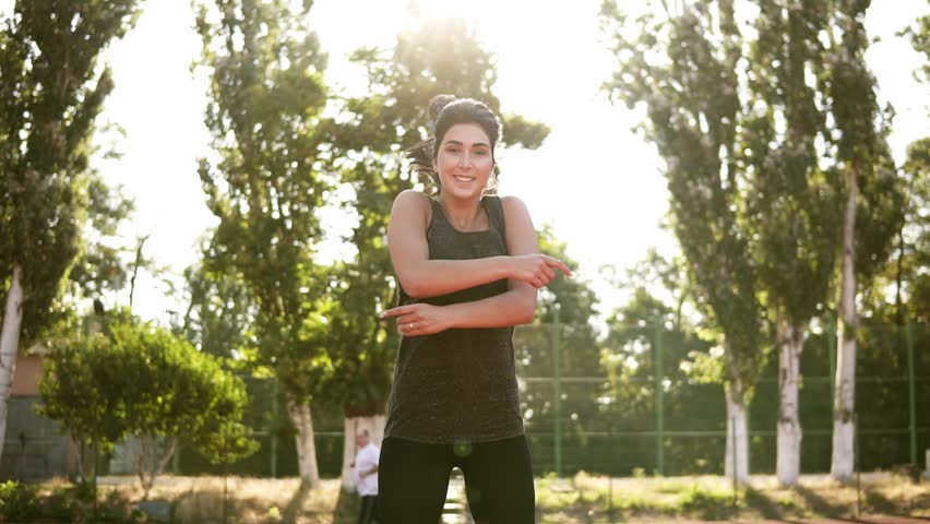 Fitness, sporty woman exercising outdoors on the stadium. Happy brunette woman doing jumping jack or star jump exercise outdoors